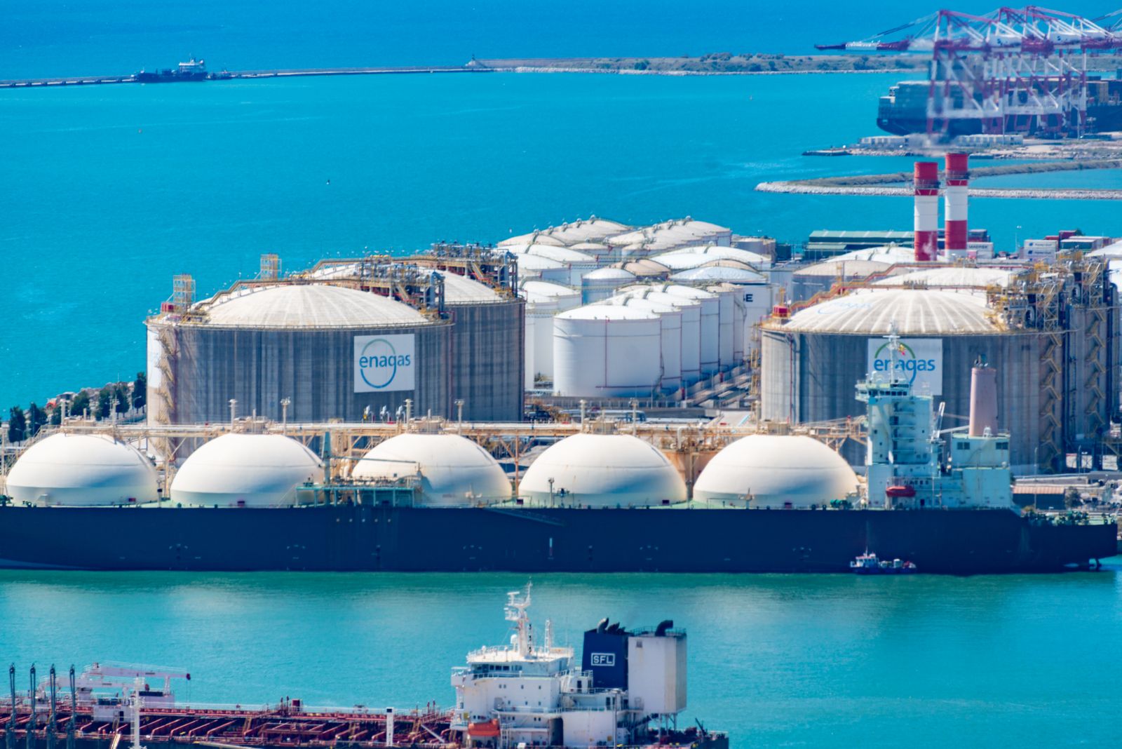 Buque metanero de gas natural licuado atracado en una terminal portuaria industrial al atardecer