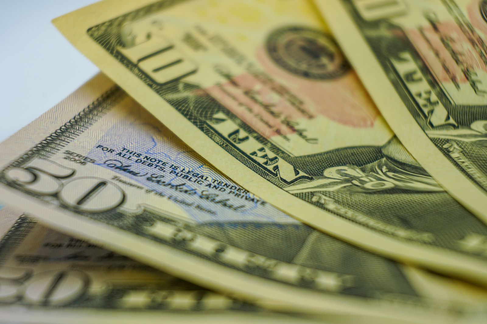 Billetes de dólar y monedas frente a una pantalla con cotizaciones de mercado