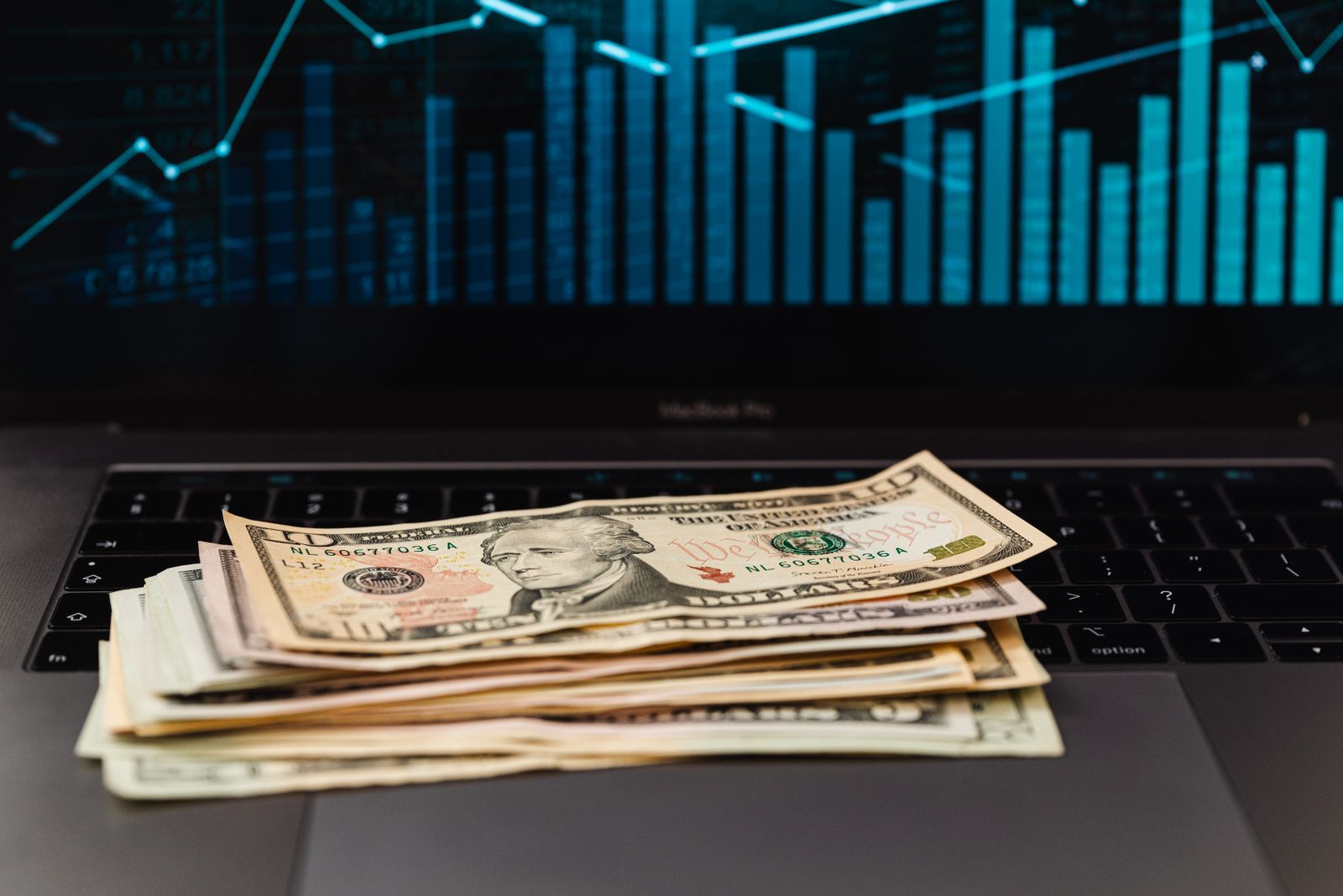 Billetes de dólar frente a una pantalla con gráficos financieros
